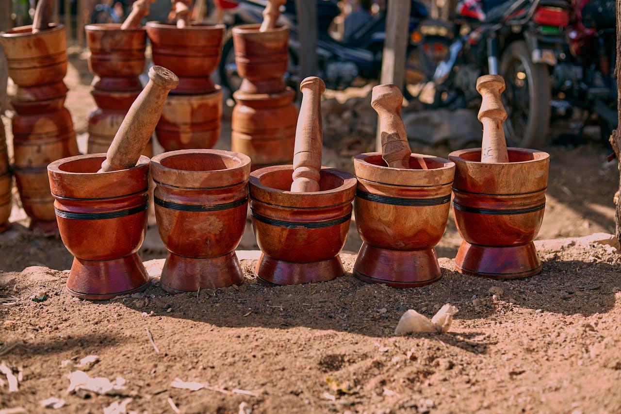 services-02 A lineup of handcrafted wooden mortars and pestles displayed on a sunny outdoor market day.