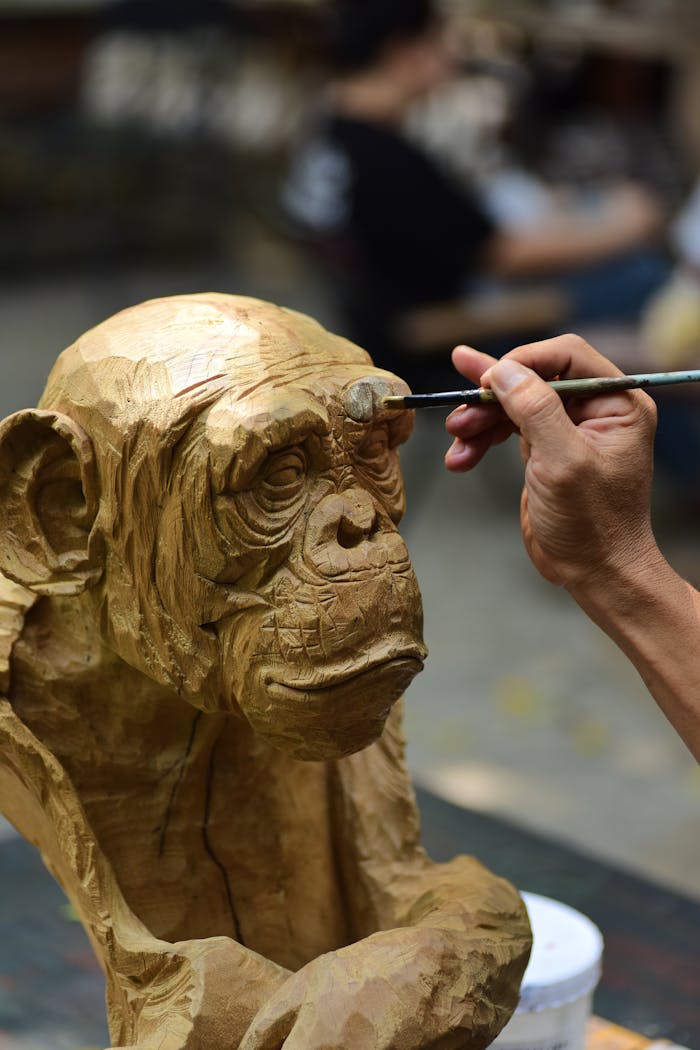 journey-02 Close-up of an artist painting a wooden ape sculpture in a workshop, showcasing creativity.